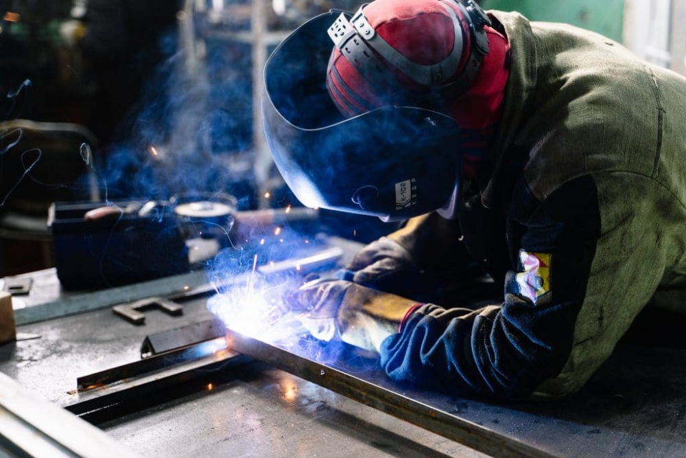 A welder works diligently on a piece of metal with sparks flying.